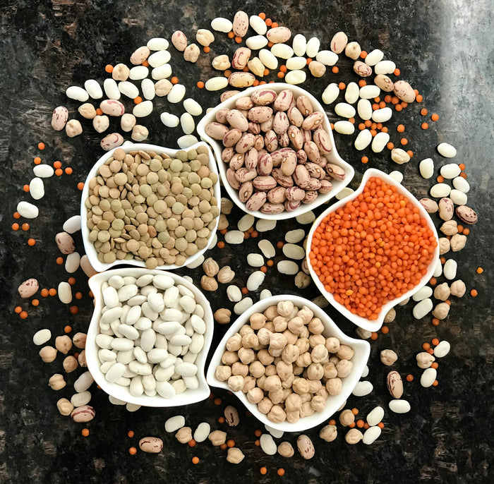Bowls of dried beans, lentils and pulses arranged on a dark surface